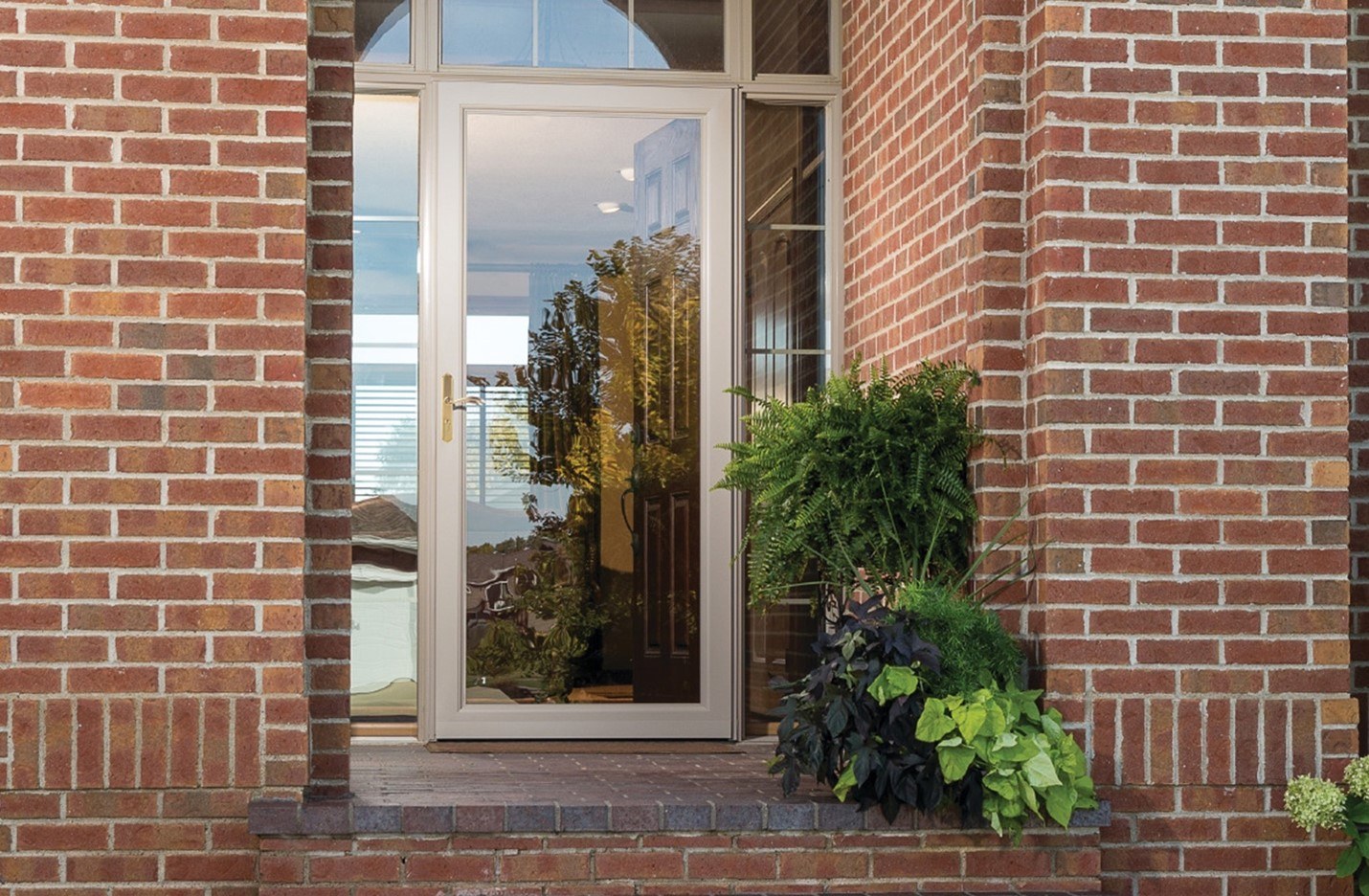 A full view storm door protects the interior of a brick house while the main entry door is open to let in light