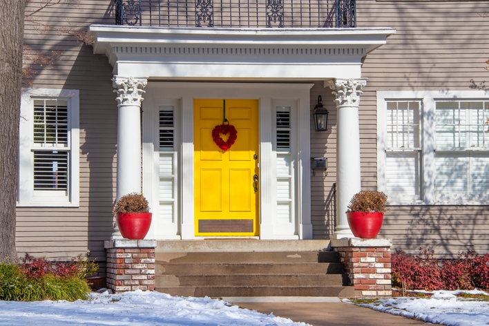 An exterior view of a house with a bright yellow entry door and white single-hung windows