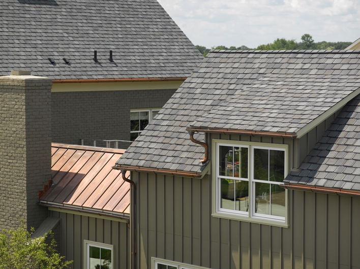 A home with a combination of types of roof materials — shingles and metal — complimented by copper-colored gutters and large, energy-efficient windows.