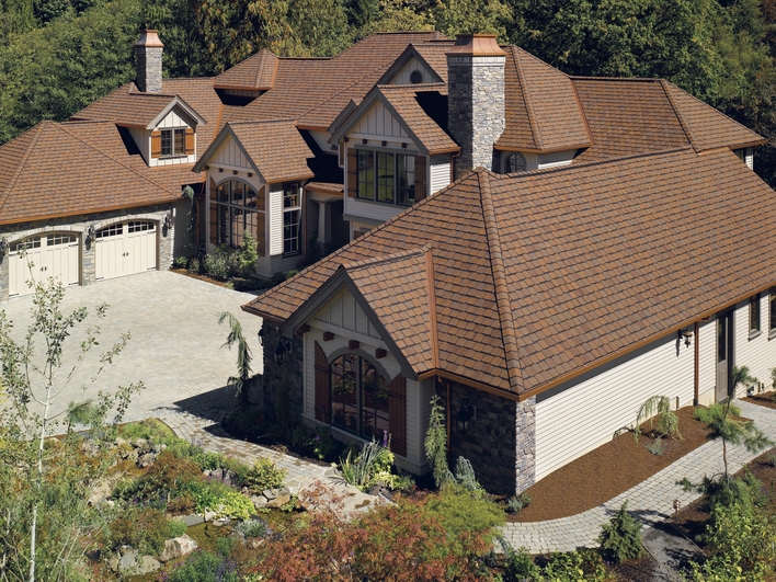 Brown shingles on the hip roof of a home with a large driveway and several architectural-shaped windows.
