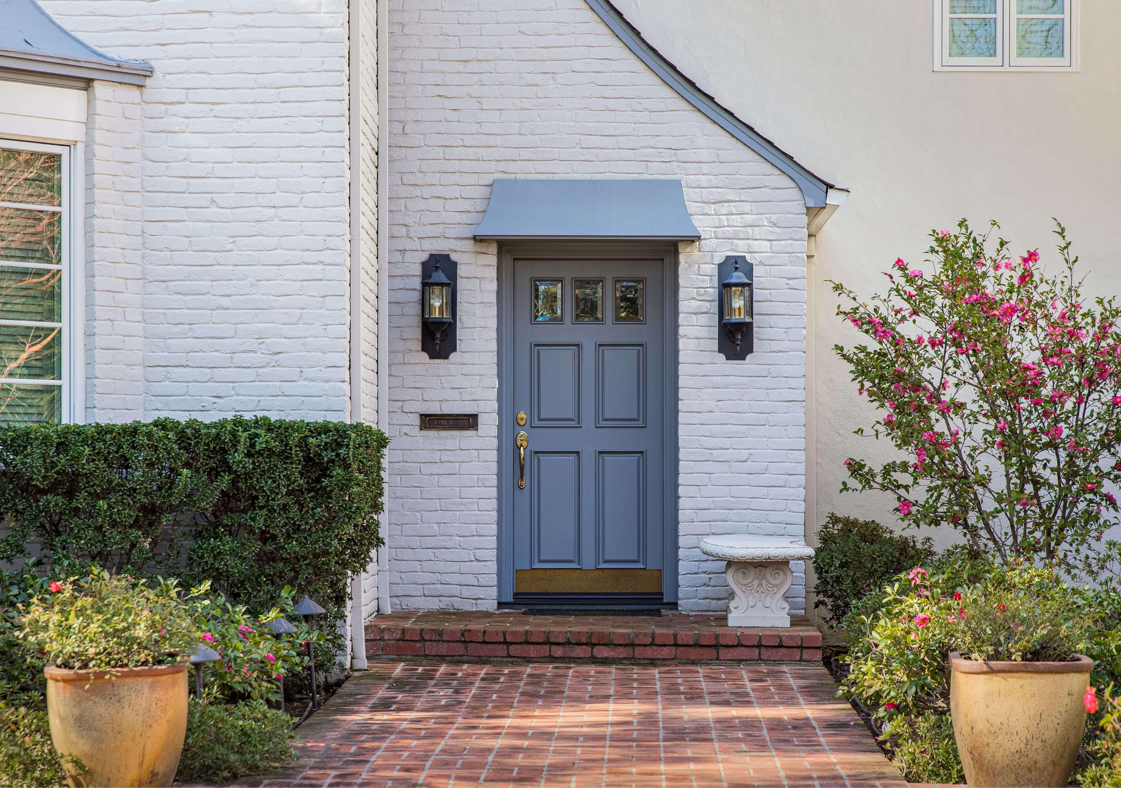 A brick walkway leading to a white brick home with a grey front door and plants