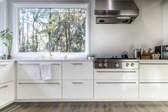 A large picture window above the kitchen sink in an all-white kitchen A large picture window above the kitchen sink in an all-white kitchen