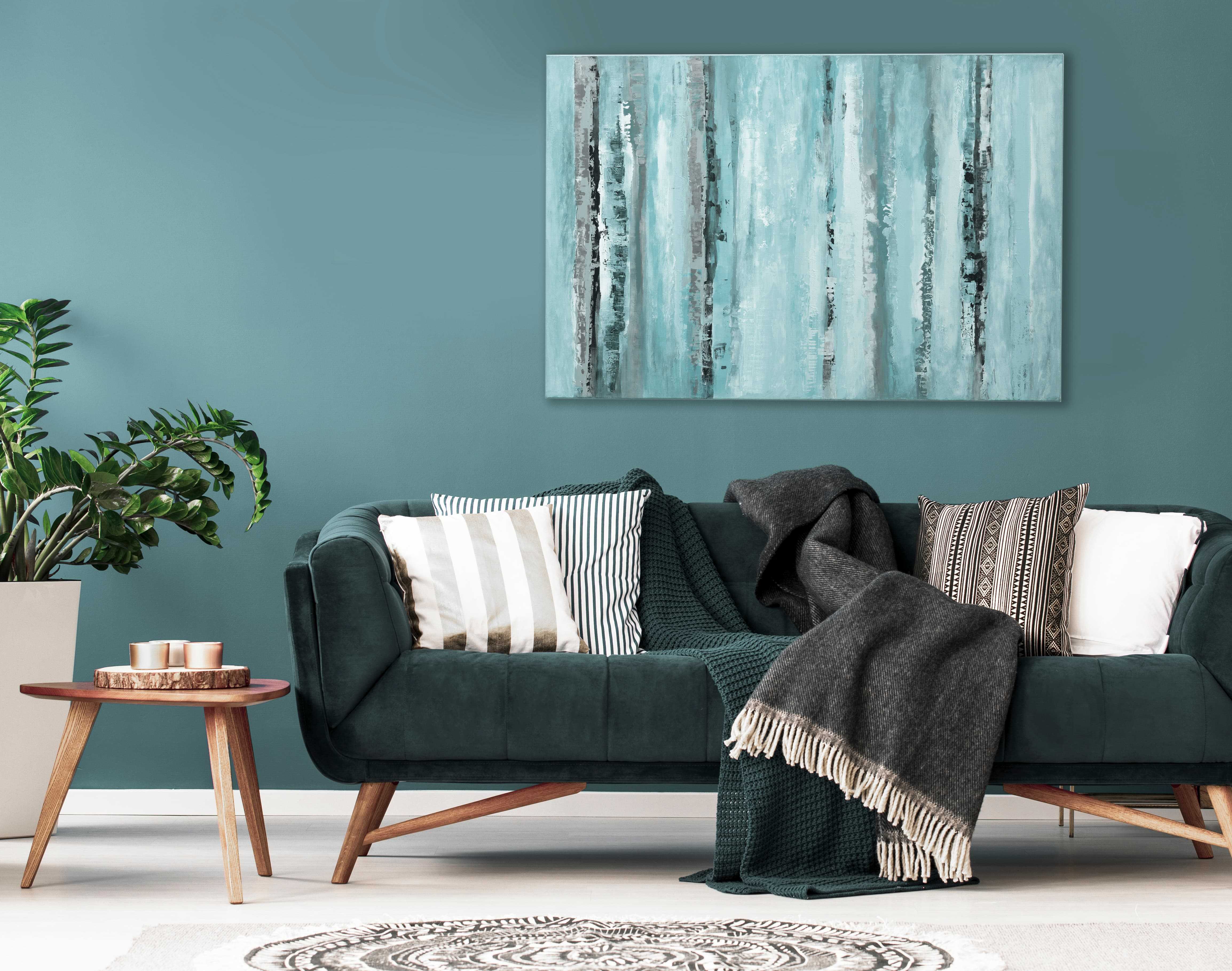 living room couch with pillows and blankets on it in front of a green wall with large artwork