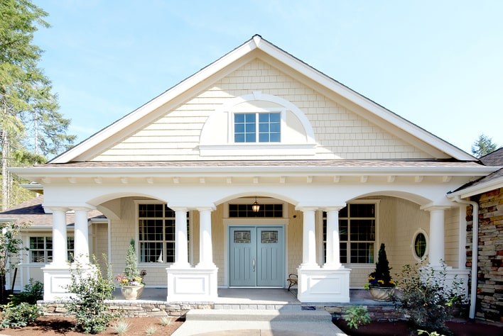 A beautifully remodeled home exterior with cream-colored vinyl siding, blue front doors, and large windows.