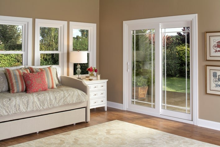 A bright sunroom with a daybed and colorful furniture that is naturally lit from a sliding glass patio door and windows along the walls.