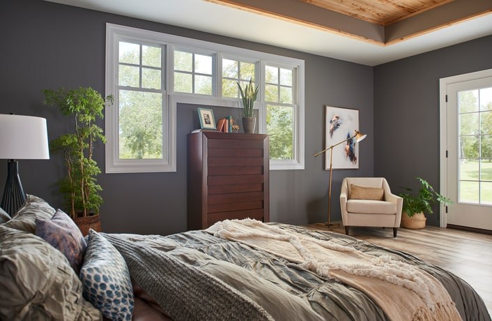 A large master bedroom with gray walls and wooden accents with windows throughout the room bringing in a lot of natural light.
