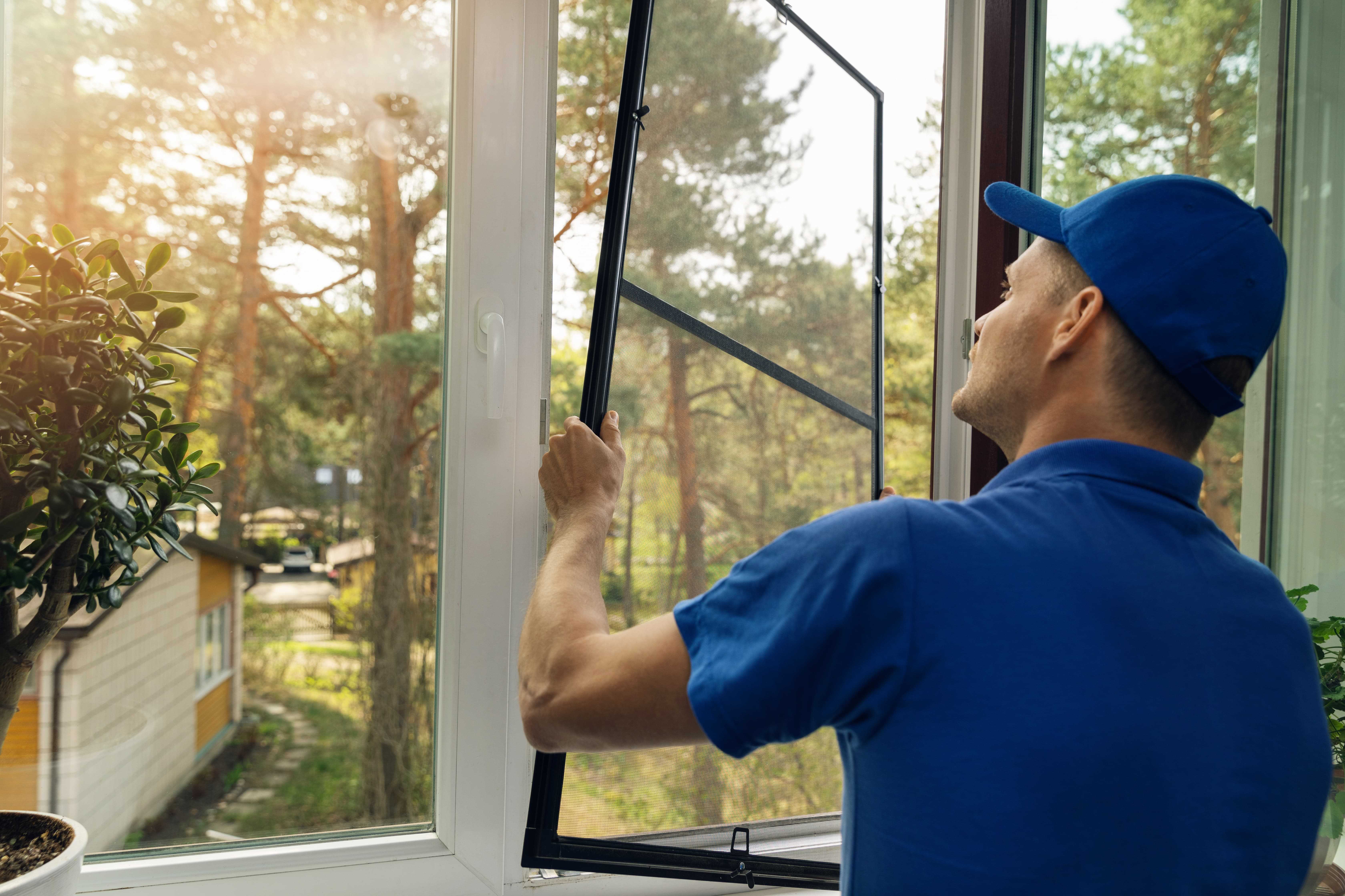 Man installing a window screen inside of a house