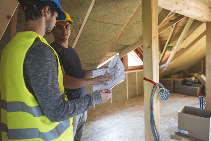 A person in a yellow vest examining the interior of a roof A person in a yellow vest examining the interior of a roof