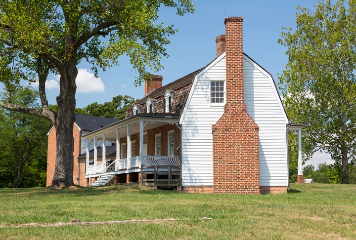 A house with a gambrel roof, large front porch, and brick chimney.