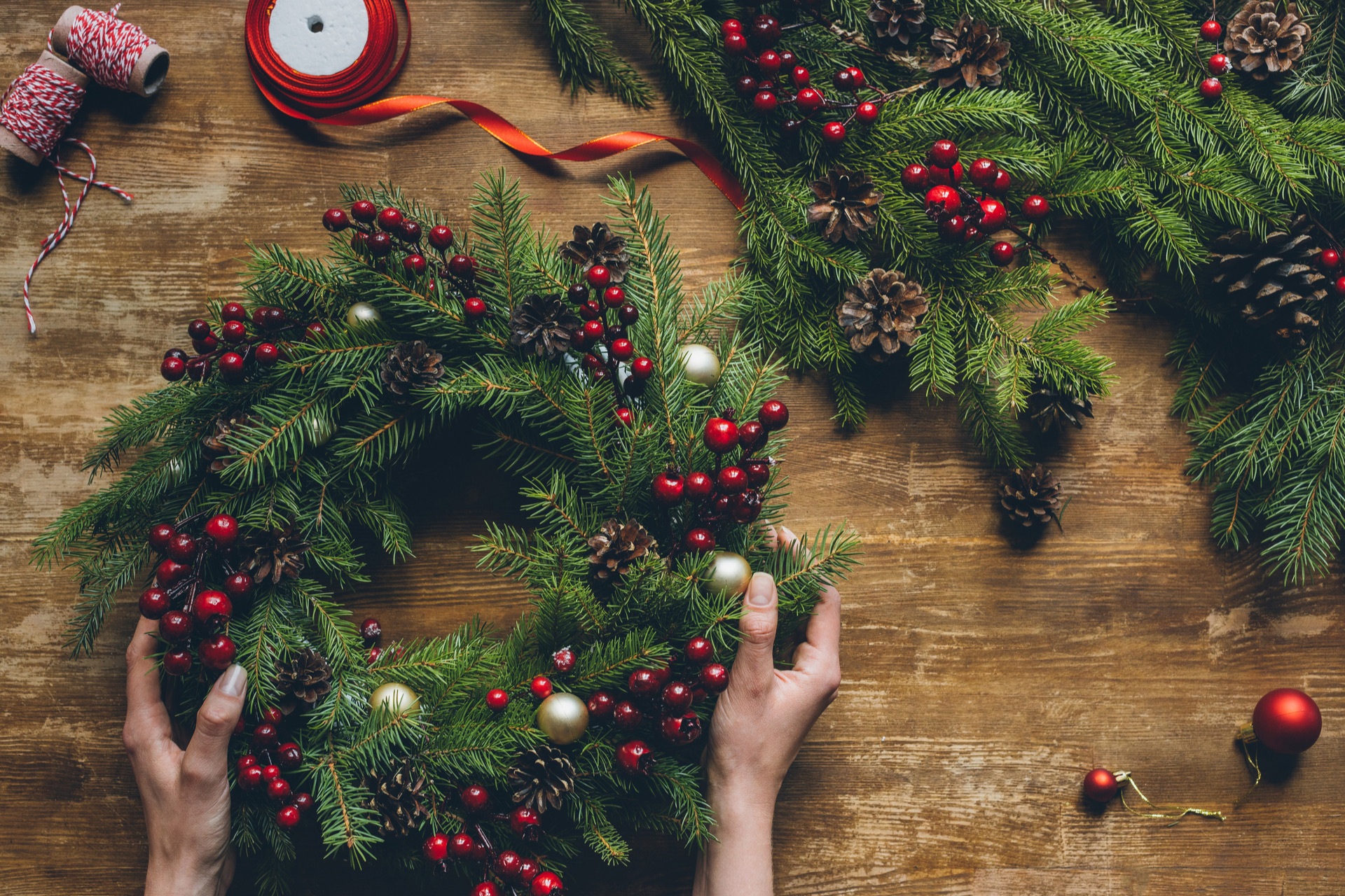 Female Hands Holding Christmas Wreath On Wooden Tabletop