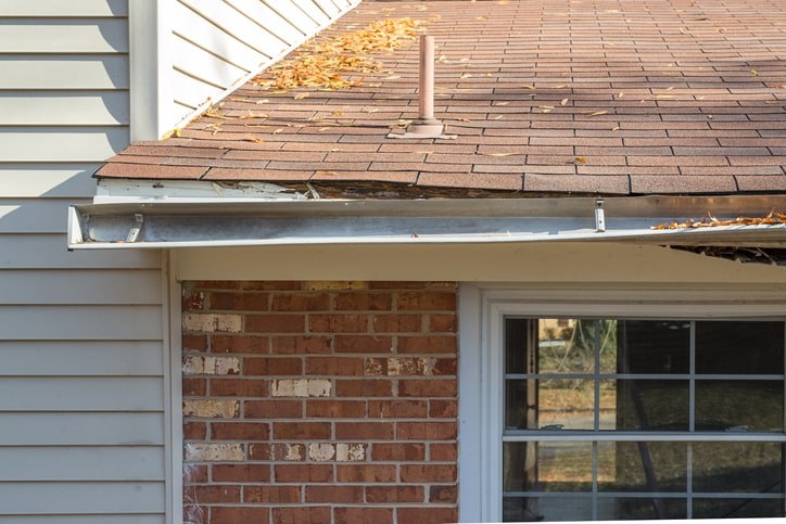 A brick house with rusty and detaching gutters