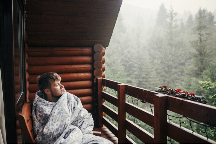 Man snuggled in blanket on porch watching the rain