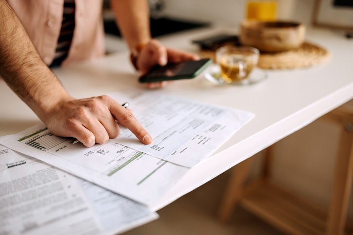 A person pointing at a bill and doing calculations on their phone