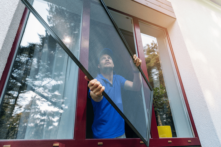 A man positioning a repaired window screen for reinstallation.