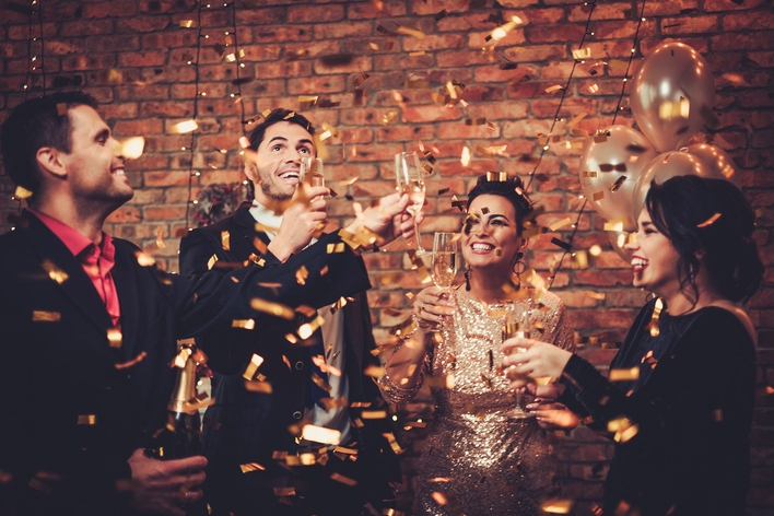Gold confetti falling on 2 men and 2 women at a new year’s eve party