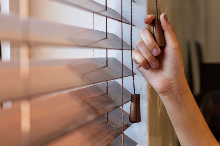A person pulling the string of wood blinds to close them. A person pulling the string of wood blinds to close them.