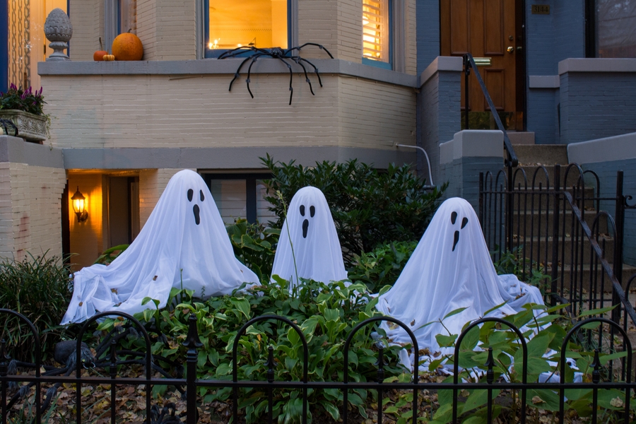 A trio of Halloween décor ghosts and a fake spider in the background outside a haunted house