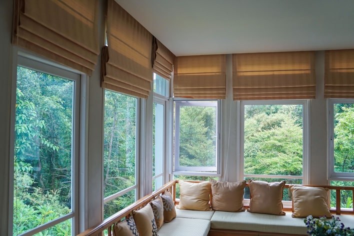 A large, neutral-toned sunroom with walls of large windows that can be covered with Roman shades. A large, neutral-toned sunroom with walls of large windows that can be covered with Roman shades.