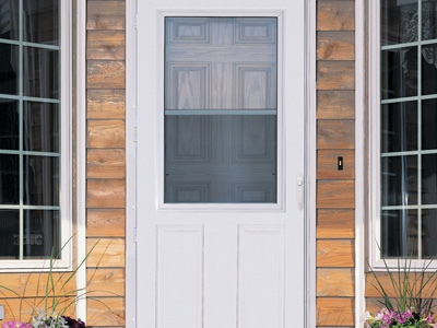 A classic-looking white storm door on a wood-paneled home.